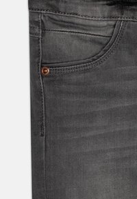 Šedé džíny z denimu s přední kapsou a bronzovým knoflíkovým akcentem, viditelným šitím a hladkou, mírně opotřebovanou texturou.