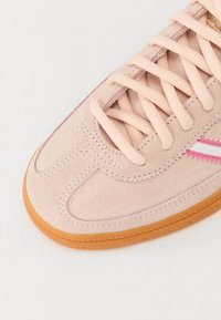Lys rosa semsket sneaker med kremfargede snører, som har et segmentert overdesign og en såle av gummigummi. Inkluderer diskrete rosa detaljer.