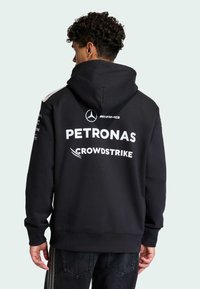 Sweat à capuche noir avec impressions de logo blanc. Comprend une poche avant et des poignets côtelés. Matière douce et confortable, conçue pour un style décontracté.