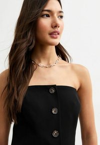 Svart strapless topp med fyra runda knappar framtill, slät textur och en figurnära design. Silverkedjehalsband som accentuerar.