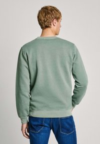Ljusgrön sweatshirt med långa ärmar, ribbade manschetter och rundad halsringning. Materialet ser mjukt och slätt ut, med en enkel design.
