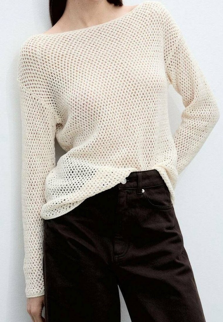 Pull crème en maille ouverte avec un design épaules dénudées, associé à un pantalon moulant marron foncé. Tissu texturé et coupe ample.