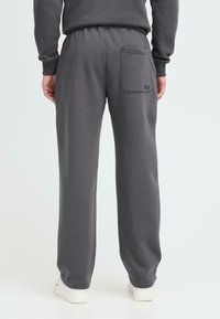Grå sweatpants lavet af blødt materiale, med elastisk talje og en baglomme med et lille logo-patch. Løs pasform over det hele.