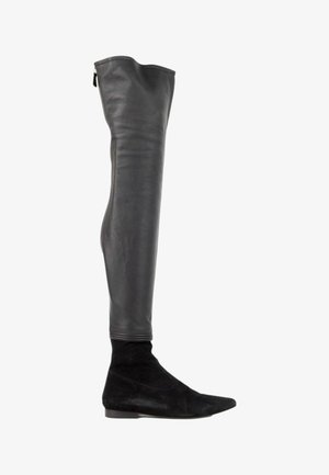 Botte noire au-dessus du genou avec une tige en cuir lisse et une partie inférieure en daim à bout pointu avec un talon bas et plat.