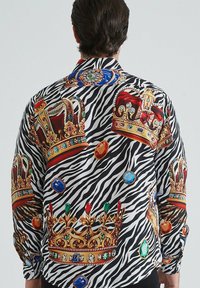 Chemise à boutons ornée d'un motif zèbre avec de grandes illustrations de couronnes colorées et de gemmes. Tissu lisse avec des accents brillants.