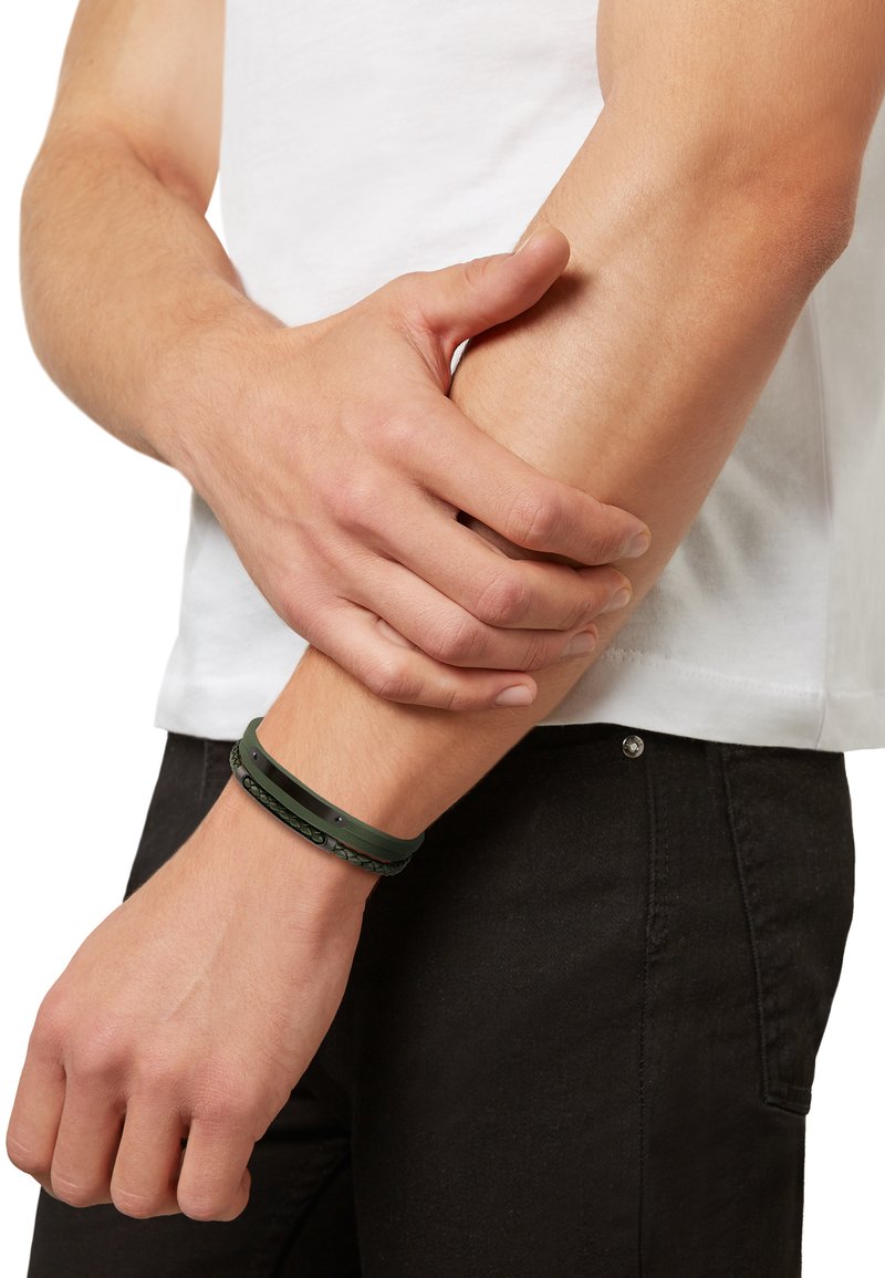Czarno-zielone opaski na nadgarstek wykonane z gumy, z teksturowanym wzorem i gładkimi akcentami, noszone na nadgarstku na tle białej koszuli.