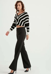 Randig svart och vit kortärmad tröja med V-halsringning, tillsammans med hög midja svarta vida byxor och svarta högklackade skor.