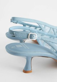 Lyseblå højhælede sandaler med en strappy design, justerbar spænde og en kontureret fodbed. Materialet ser glat og blankt ud.
