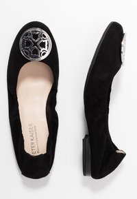 Sorte suede flade sko med en lav hæl, prydet med en rund sølvaccent på tåen. Blød tekstur og enkelt design for alsidig brug.