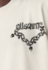 Bijela pamučna majica s crnim grafičkim dizajnom lanca s srcastim detaljima i tekstom "allsaints" integriranim unutar dizajna.