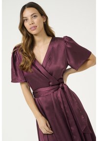 Burgundy wrap dress with short puff sleeves, textured fabric, and a tied waist detail. Features a deep V-neckline and flowing skirt.