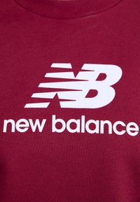 Sweatshirt bordeaux arborant un grand logo "N" blanc avec des lignes de vitesse et le texte "new balance" en lettres blanches grasses en dessous.
