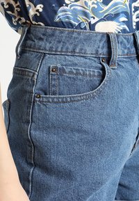 Jeans de mezclilla con cinturilla de altura media, diseño de cinco bolsillos, color azul claro con costuras contrastantes y tela texturizada.