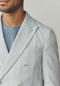 Hellgrauer, doppelt knöpfbarer Blazer mit vertikalen Nadelstreifen, aus strukturiertem Stoff; verfügt über zwei Knöpfe und eine Brusttasche.