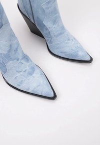 Botas de tobillo de denim azul claro con punta afilada, tacón de cuña negro y detalles de costura en un diseño curvado a lo largo de los lados.