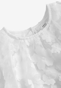 Hvid bluse med transparent stof og 3D blomsterapplikationer, rund halsudskæring og Next-mærke på bagkraven.