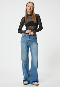 Haut long à manches longues en voile noir associé à un jean large bleu clair. Le jean présente une taille haute et un léger dégradé, avec une coupe décontractée.