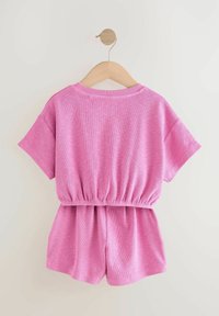 Lyserød bomuldsoutfit med korte ærmer og en elastisk talje. Toppen har en rund halsudskæring, og shortsene har en afslappet pasform.