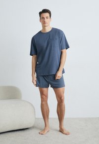 Donkerblauw katoenen T-shirt met korte mouwen en een zak, gecombineerd met bijpassende shorts. Ontspannen pasvorm, minimaal ontwerp op een gestructureerd oppervlak.
