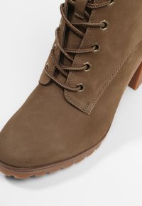 Bottine en daim marron avec un bout arrondi, dotée de lacets marron, d'œillets métalliques et d'un talon carré. La semelle est texturée pour une meilleure adhérence.