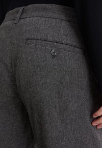 Gray tailored pants with a textured fabric, featuring a back pocket secured by a button, and a smooth waistband.