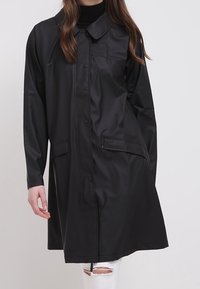 Svart vattentät rock med krage, knäppning framtill, två framfickor och midjelång design. Mjuk textur och ledig passform.