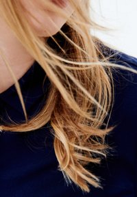 Lang, golvend blond haar verbergt gedeeltelijk een donkerblauwe stof, wat een zacht textuurcontrast creëert tegen de gladde achtergrond.