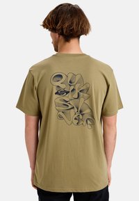 Camiseta de algodón verde oliva con un gran gráfico de arte lineal negro en la parte trasera, con formas abstractas y curvas. Corte relajado.