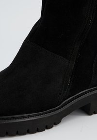 Black suede ankle boot with a textured finish, reinforced stitching along the seams, and a rugged rubber sole with a prominent tread pattern.