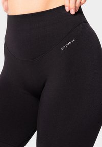 Leggings neri con una vita alta, realizzati in un tessuto testurizzato. Presentano un logo bianco sull'anca e un design liscio e senza cuciture.