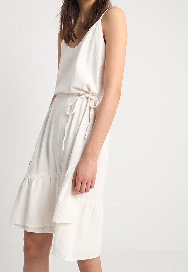Vit klänning i linblandning med avslappnad passform, justerbart knytdetalj vid midjan och utsvängd nederkant. Har spaghettiband och en enkel design.