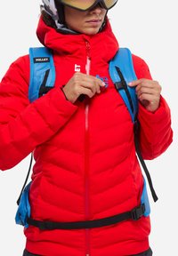 Rote isolierte Jacke mit Reißverschluss, Fleece-Futter und blauen Trägern. Verfügt über ein Logo und einen verstellbaren Bund für einen sicheren Sitz.