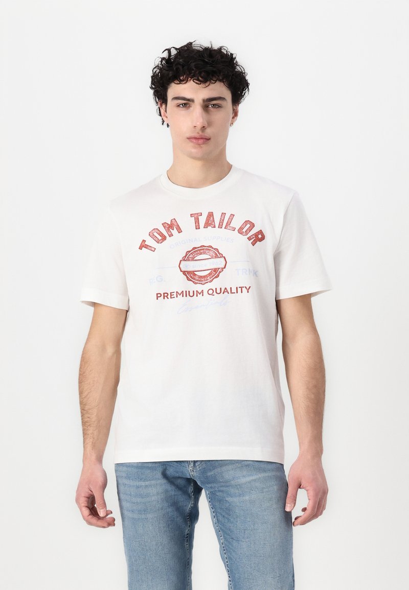 Hvit bomull T-skjorte med korte ermer, med rød tekst "TOM TAILOR" og dekorative grafiske elementer. Jevn tekstur, klassisk passform.