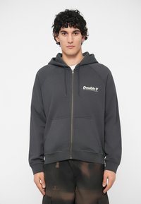 Γκρι φούτερ με φερμουάρ, που διαθέτει κουκούλα και μπροστινές τσέπες, με το λευκό λογότυπο "Double V" στο αριστερό μέρος του στήθους. Μαλακό ύφασμα με απαλό υφή.