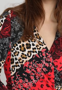 Buntes Oberteil mit einem Patchwork-Design, das Blumen-, Leoparden- und Paisleymuster in Rot, Schwarz, Weiß und Beige zeigt. Weicher Stoff.