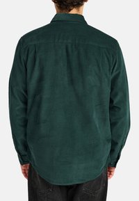 Dark green corduroy shirt with a button-down collar, long sleeves, and a rounded hem, featuring a subtle texture and back yoke seam.