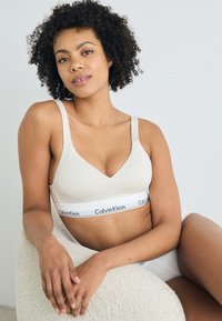 Μπεζ βαμβακερό bralette με σχέδιο V-neck και φαρδιές τιράντες, που διαθέτει μια λωρίδα με λογότυπο Calvin Klein σε μαύρο και άσπρο στο κάτω μέρος.
