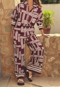 Tenue à motifs bordeaux avec des rayures blanches ; haut à manches longues ample et pantalon à jambes larges. Accessoirisée avec des sandales plateformes noires.