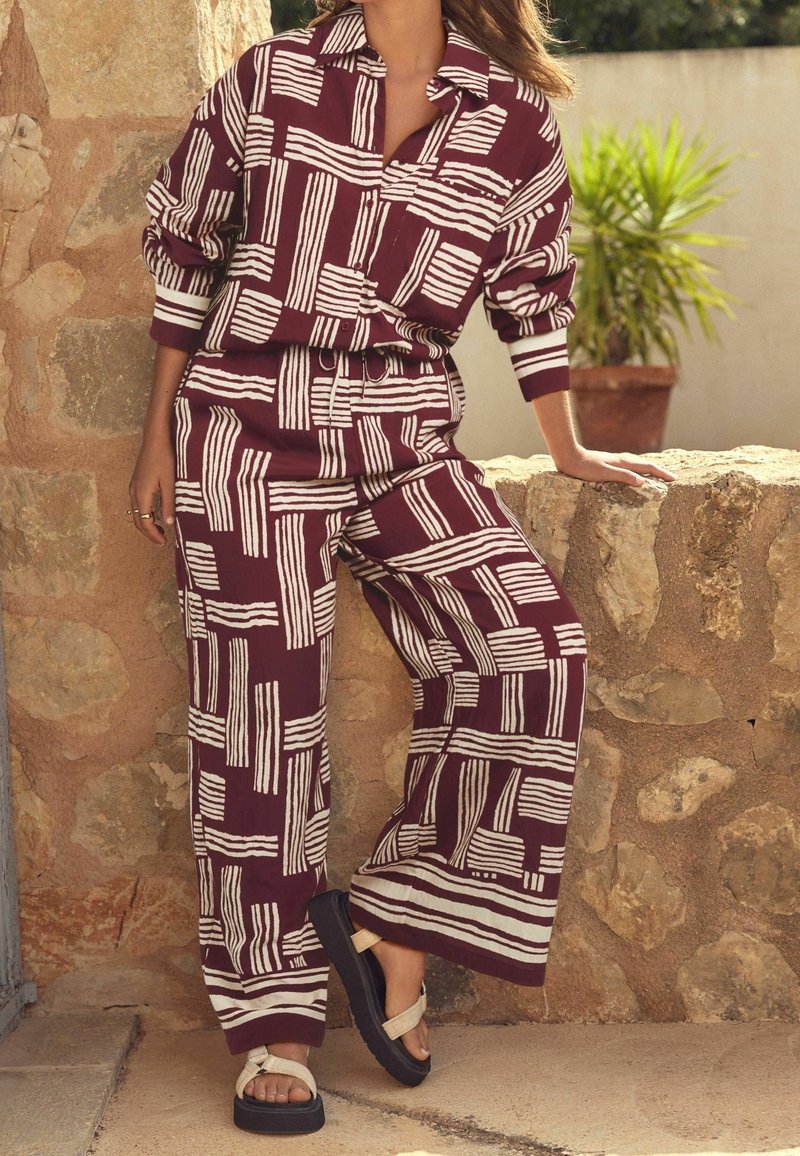 Tenue à motifs bordeaux avec des rayures blanches ; haut à manches longues ample et pantalon à jambes larges. Accessoirisée avec des sandales plateformes noires.