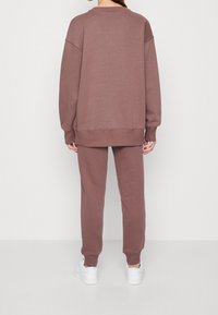 Sudadera color topo y joggers a juego, hechos de un tejido suave; ajuste relajado, puños y cintura acanalados; combinados con zapatillas blancas.