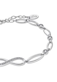 Bracelet argenté avec des maillons ovales entrelacés, des pierres claires rondes et un design en forme d'infini, avec une petite étiquette de marque.