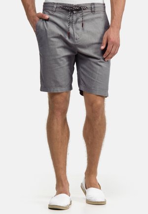 Homme portant un short gris à cordon et des chaussures blanches sans lacets, debout avec les mains détendues le long du corps.