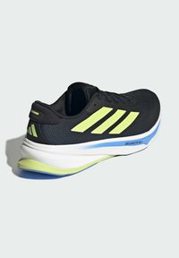 Zapatilla deportiva negra con acentos amarillos, parte superior de malla y una suela blanca acolchada con detalles en azul y verde, etiquetada como "DREAMSTRIKE".