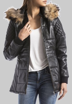 Zwarte leren jacket met gevoerde mouwen, bont-gevoerde capuchon, rits sluiting en geribbelde manchetten, gecombineerd met een witte top en blauwe jeans.