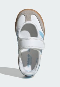 Biele a šedé tenisky s modrým akcentom, s nastaviteľným pásikom na suchý zips a textúrovanou semišovou špičkou, umiestnené na gumennej podrážke.