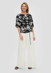 Zwart-witte bloemenblouse van zachte stof, met een losse pasvorm, brede mouwen en een gestrikte taille. Gecombineerd met witte wijde broeklegs.