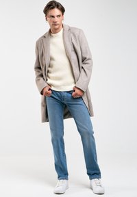 Abrigo gris claro, suéter de canalé crema y jeans de mezclilla azules. Zapatillas blancas complementan el atuendo. Textura suave, diseño a medida.