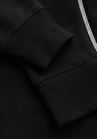 Tela de sudadera negra con puños de canalé. Textura suave con un detalle frontal con cremallera. Enfoque en primer plano en la construcción de la manga y la costura.