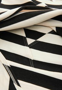 Zwart en crème gestreepte stof met driehoekige patronen, voorzien van zichtbare stiksels en een zachte, gladde textuur.