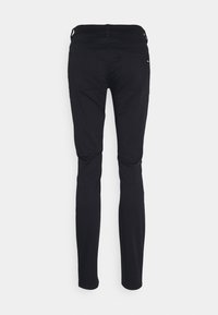 Svarta slim-fit byxor med en slät yta, med en midja i mellanhöjd och bakfickor, sedda bakifrån.